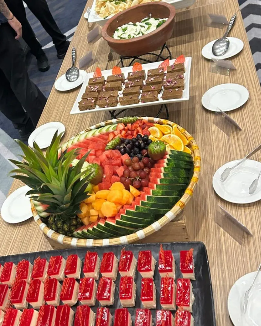 A long catering buffet with a carved fruit platter and red jelly desserts