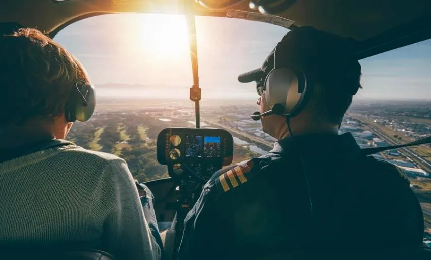 Student and pilot in a helicopter cockpit flying over the city at sunrise