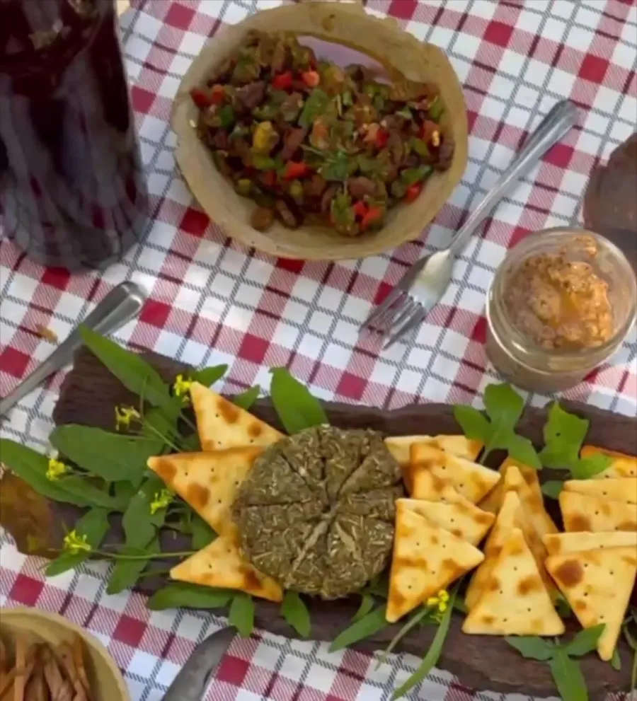 A wild-foraged feast of herb spreads, flatbread and fresh greens on a gingham picnic table