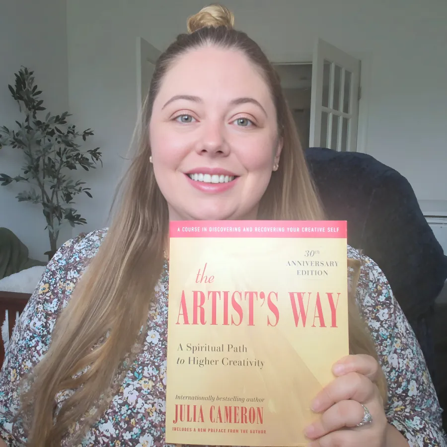 Katie smiling, holding The Artist's Way book by Julia Cameron.