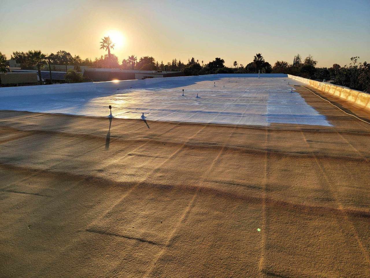 Commercial spray foam roof in Bakersfield at sunset, with bare foam in front and the finished white coating behind