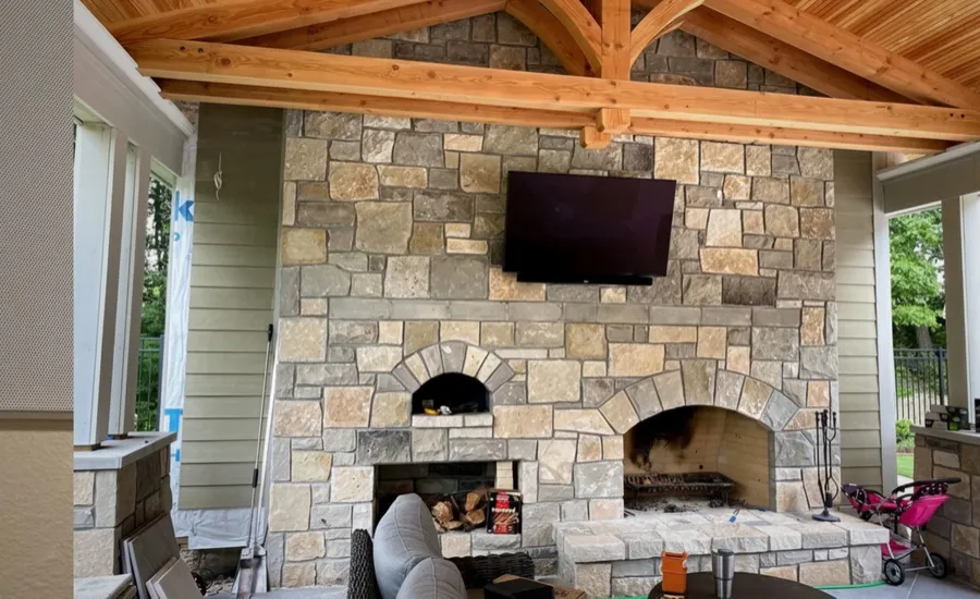 Outdoor TV above a stone fireplace on a covered patio