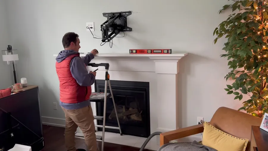 Technician installing a TV mount above a white fireplace