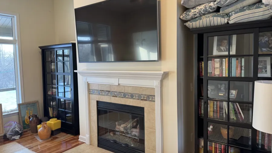 TV above a tile fireplace between dark bookcases