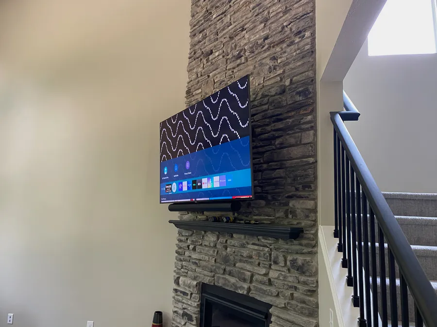 TV mounted on a stacked stone fireplace beside a staircase