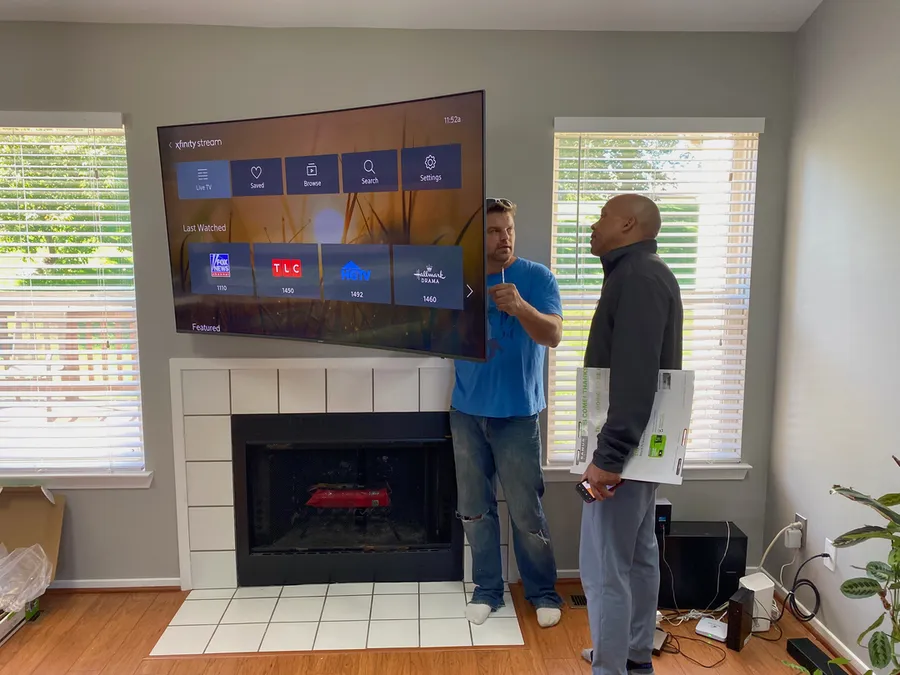 Two installers lifting a TV onto its mount above a fireplace