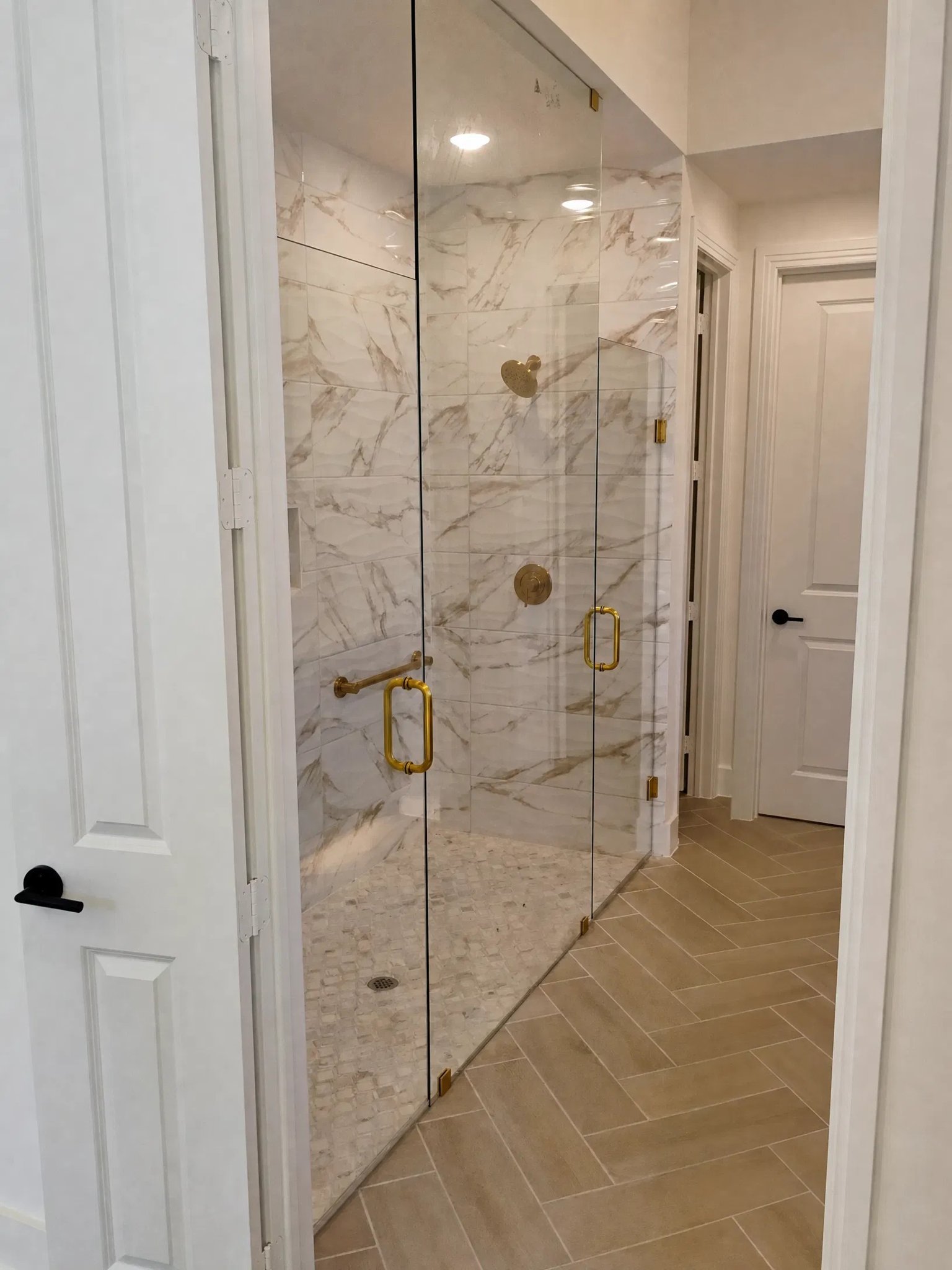 Brass-framed shower doors over herringbone tile