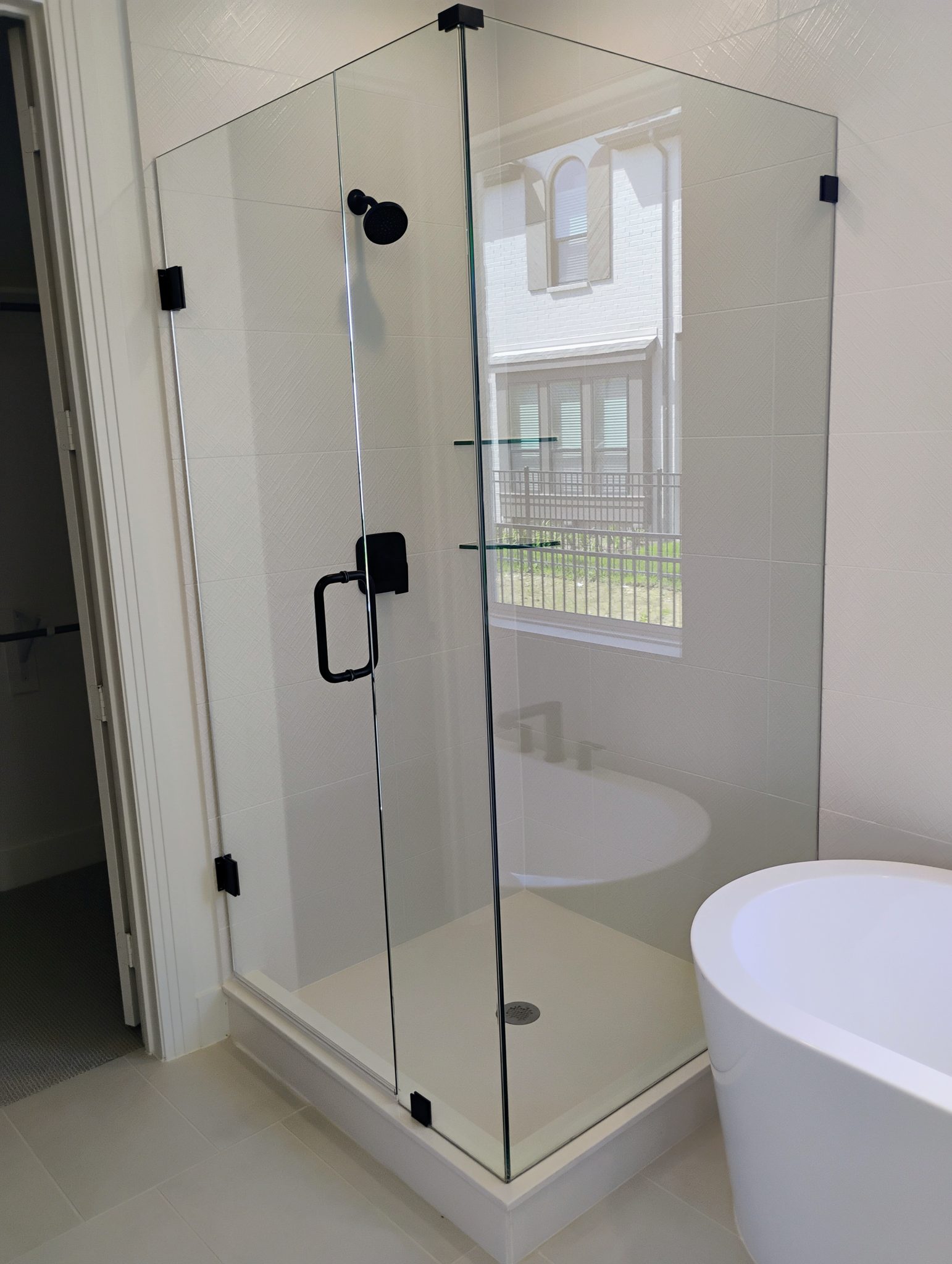 Frameless corner shower with black hardware next to a tub