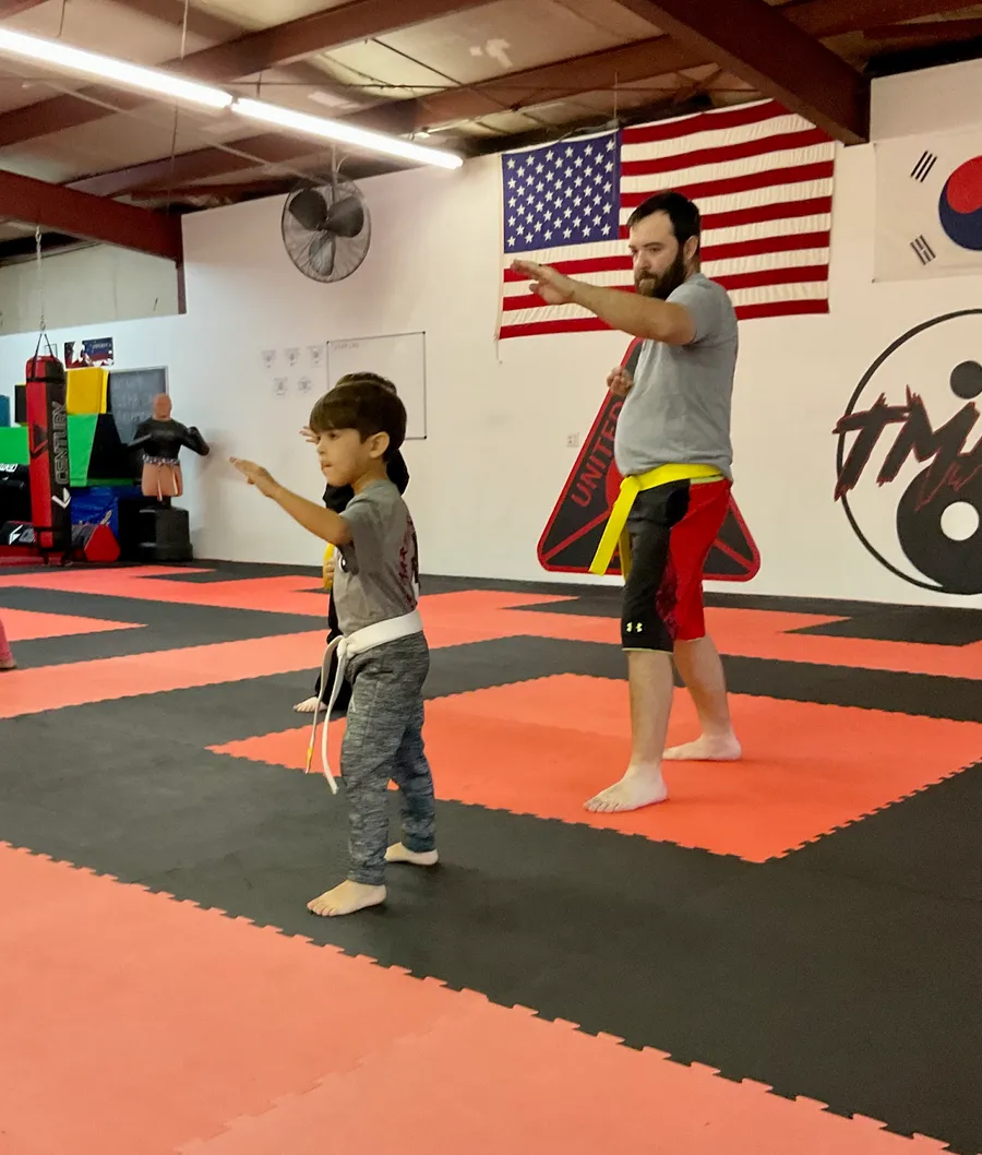 A father and young son practicing a punch together on the mats