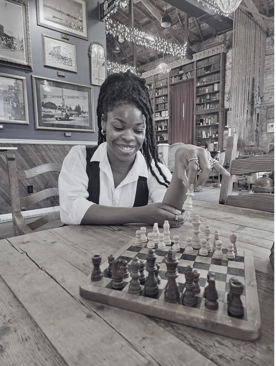 AJ smiling over a chess board, hand on a piece mid-move