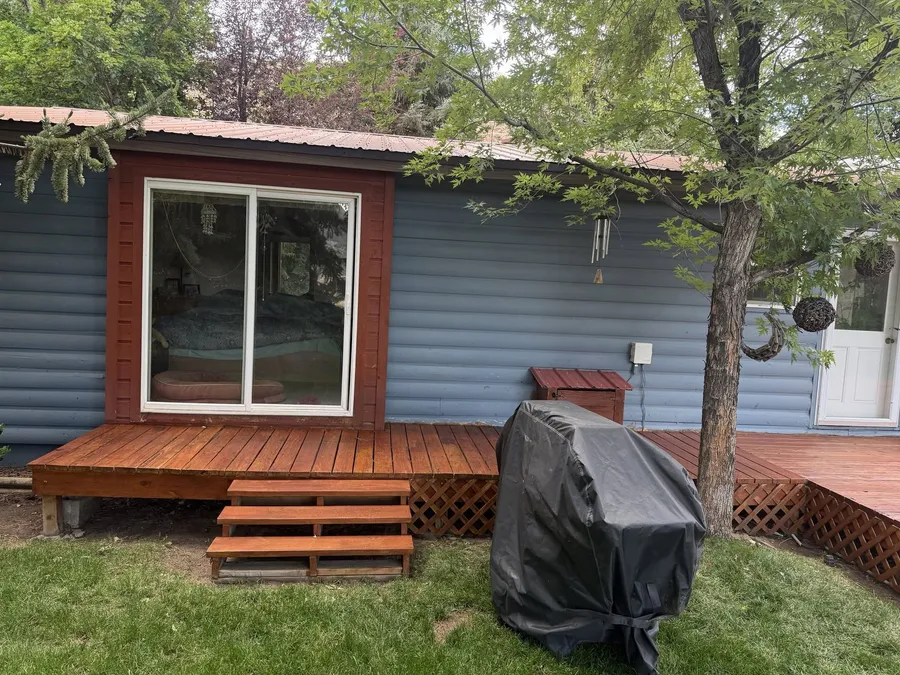 Stained deck along the back of a blue house with new wooden steps below a sliding door