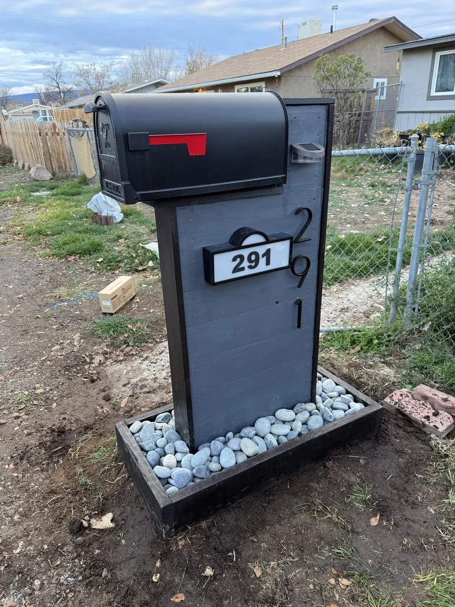 Custom gray and black mailbox column with large house numbers, a lit number sign and a river rock base