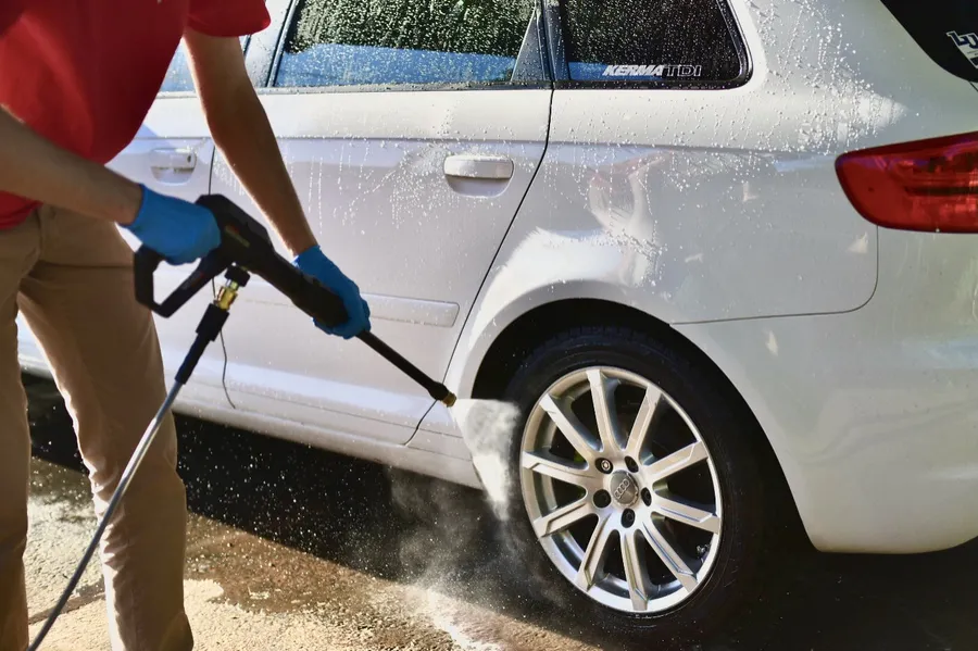 Technician rinsing a white car wheel during a hand wash