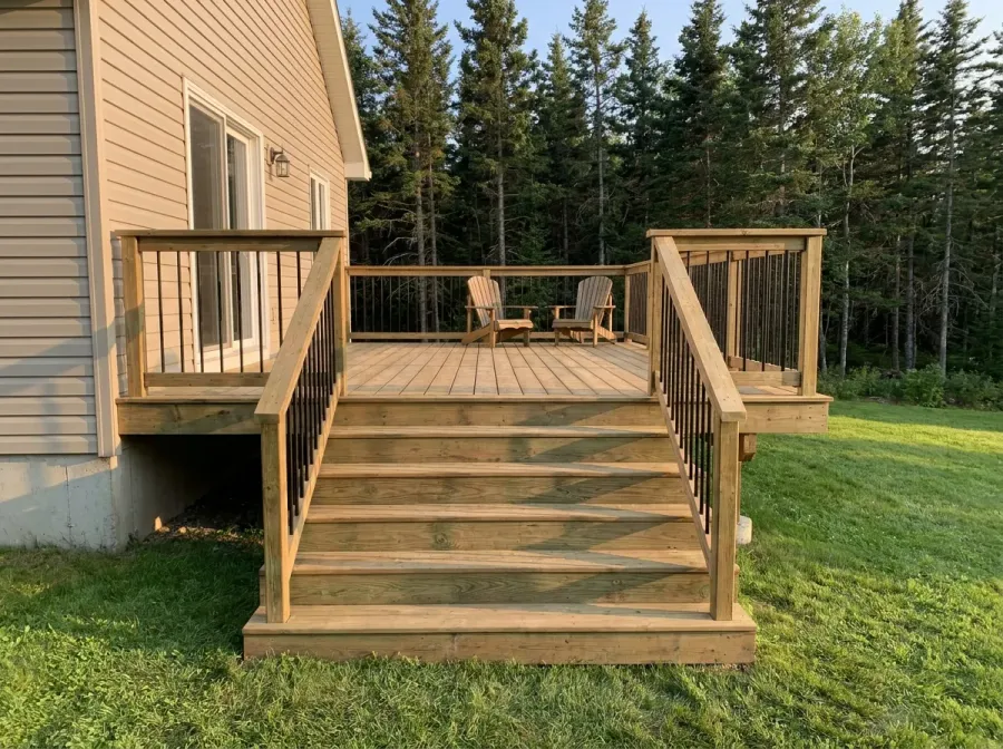 New pressure treated wood deck with wide stairs and black metal balusters, spruce forest behind