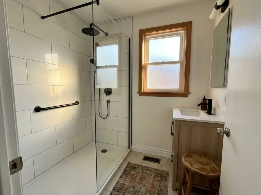 Renovated small bathroom with a walk-in shower, glass panel, black fixtures, grab bar and wood vanity