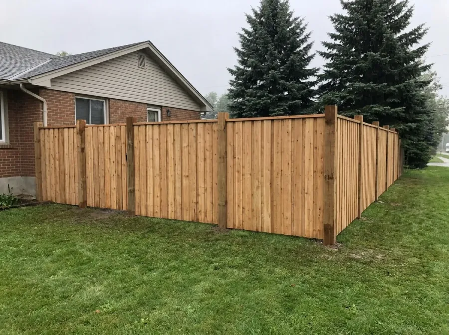 New cedar privacy fence with tall posts beside a brick and vinyl-sided house