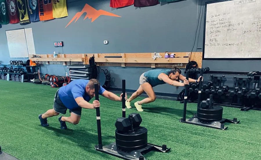 Coach and member doing sled pushes on the turf