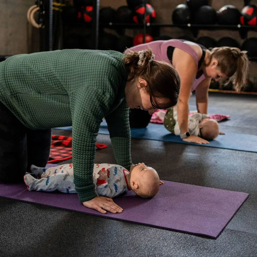 A mom doing a coached floor exercise with her baby lying on the mat in front of her