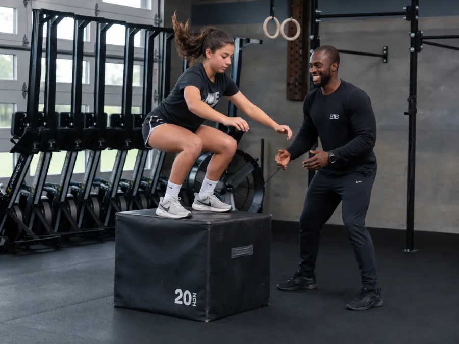 A teenage athlete box jumping while Myles coaches