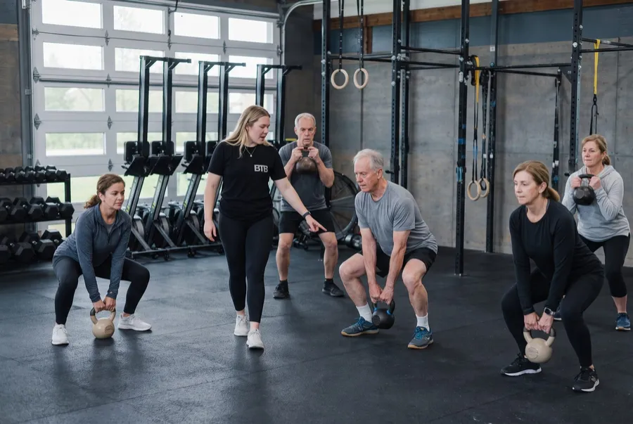A coach leading a small group of adults through kettlebell squats