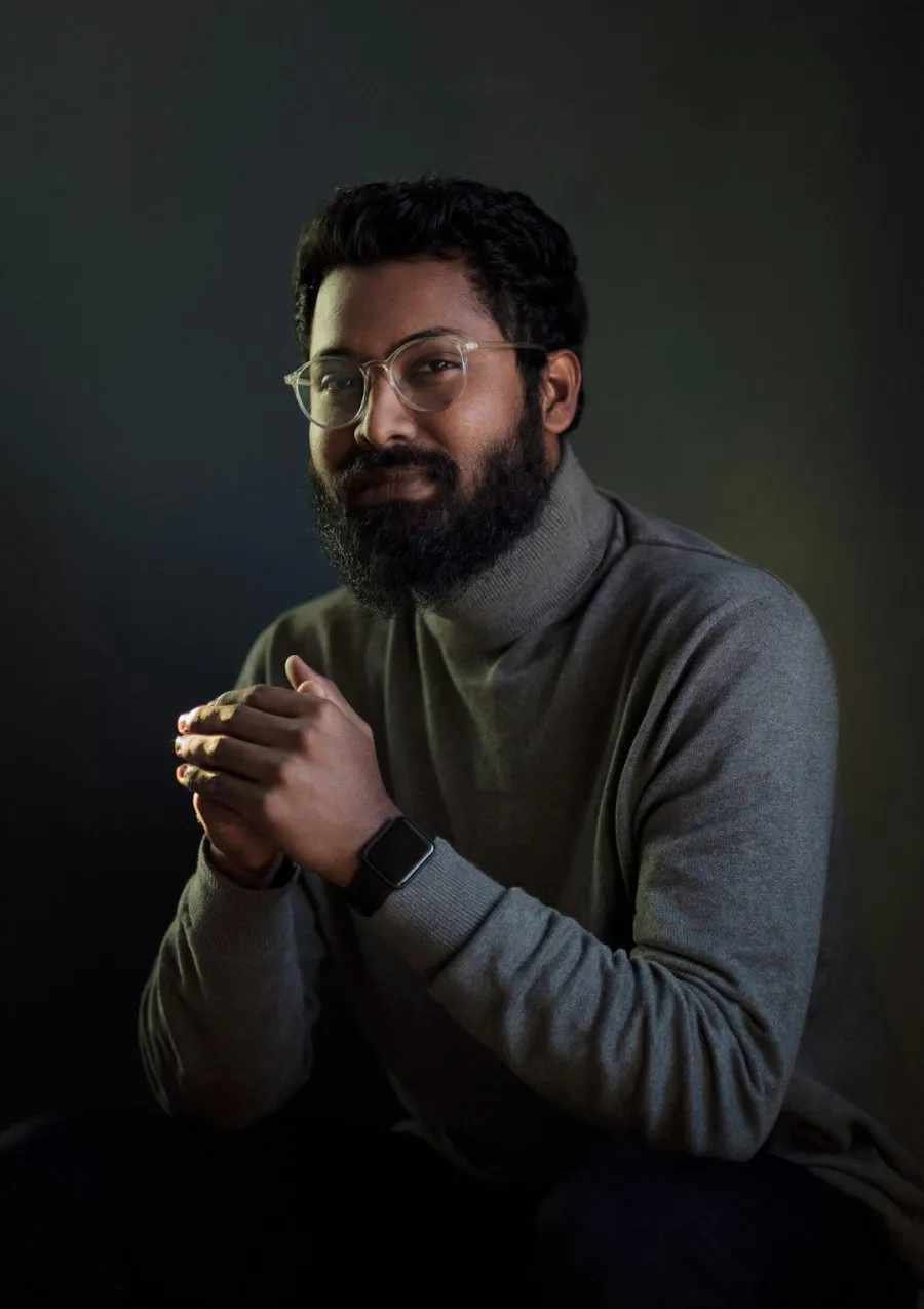 Portrait of a bearded man in a gray turtleneck photographed against a plain wall