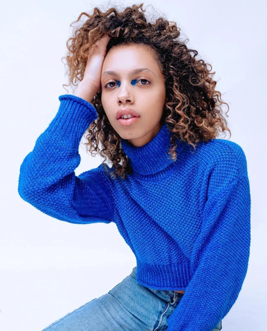 Personal brand portrait of a woman in a blue knit sweater with curly hair against a pale blue backdrop