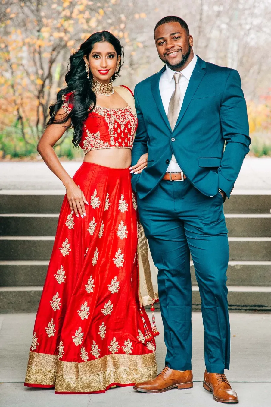 Couple in a red lehenga and teal suit on venue steps at their wedding