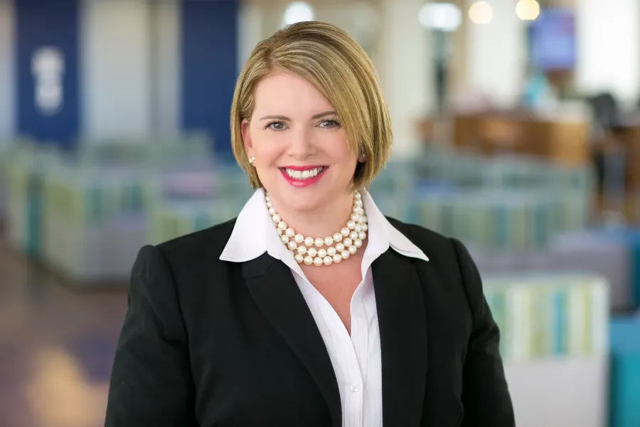 Corporate headshot of a woman in a black blazer and pearls in a modern office