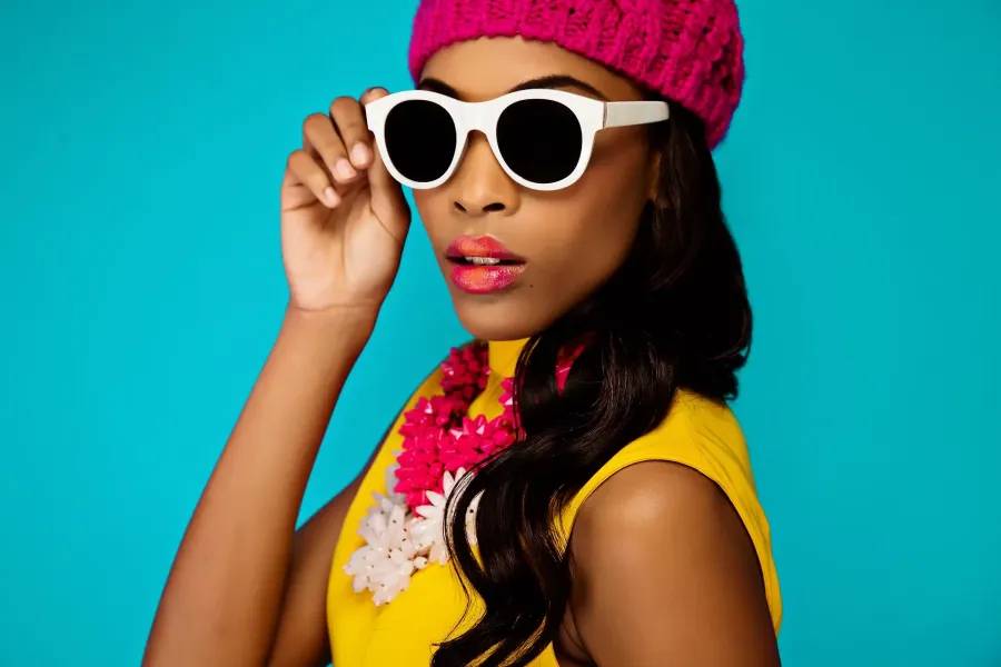Model in white sunglasses and a pink beret against a teal backdrop for a colour campaign