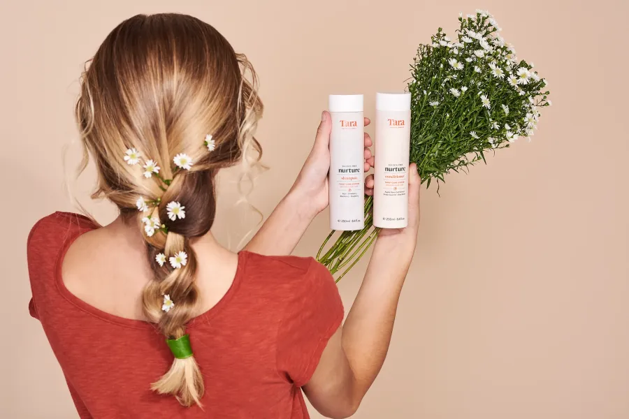 Model with a flower-studded braid holding hair care bottles for a Tara Brands campaign