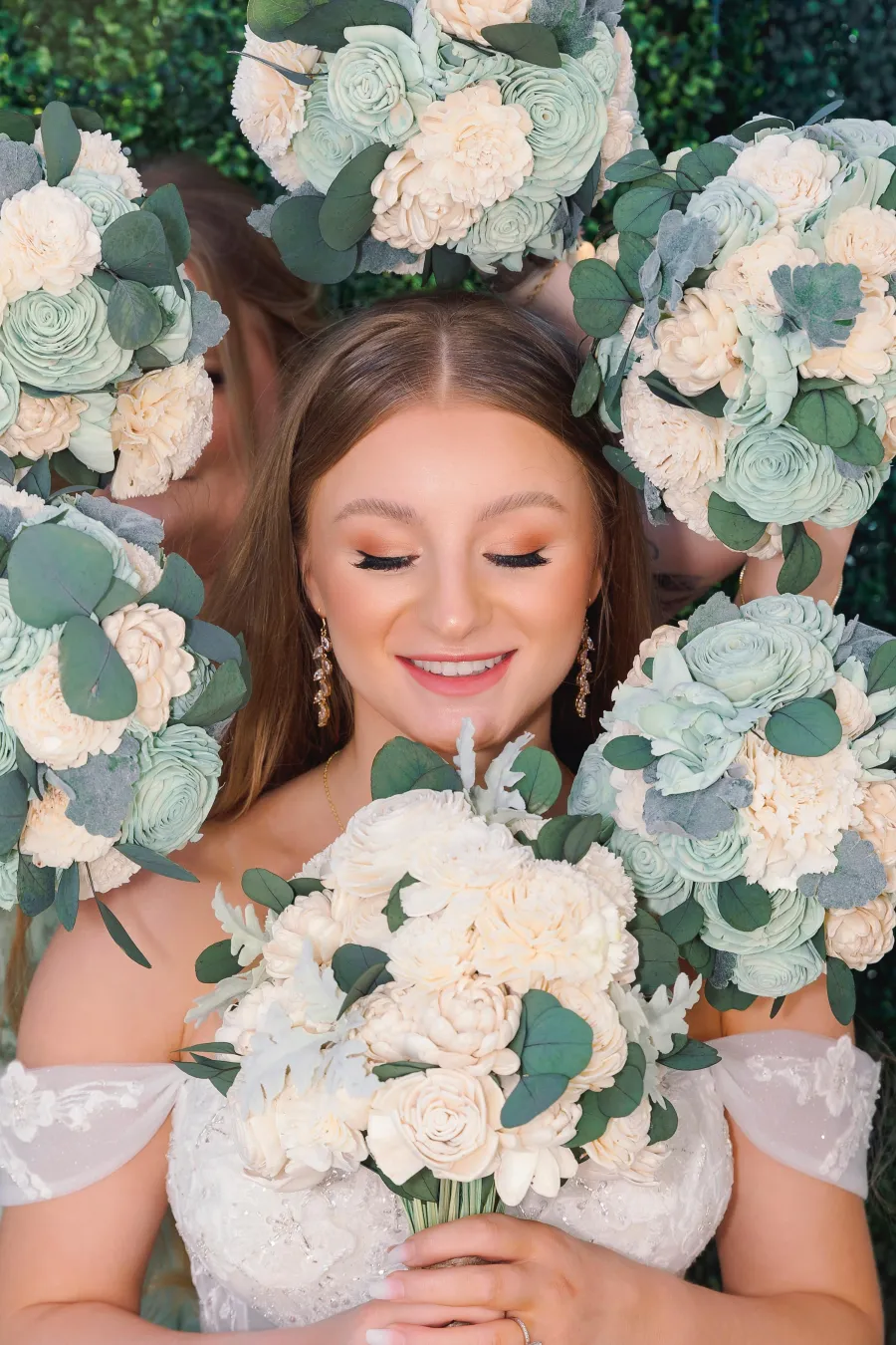 Bride smiling up at the camera surrounded by white rose and eucalyptus bouquets