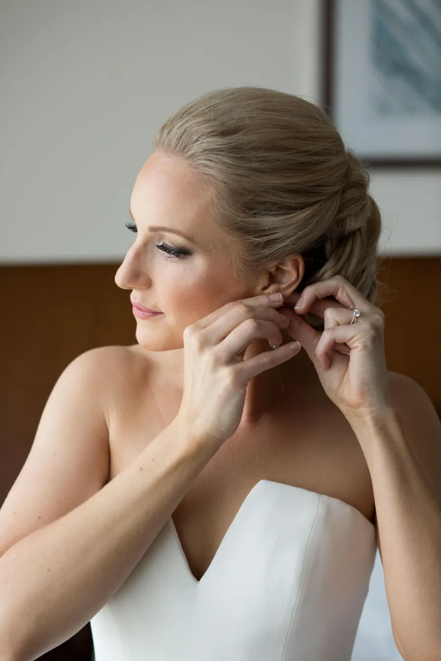 Bride fastening her earring, hair in a smooth low bun