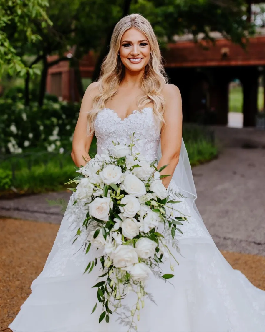 Blonde bride with a cascading white bouquet in a garden courtyard