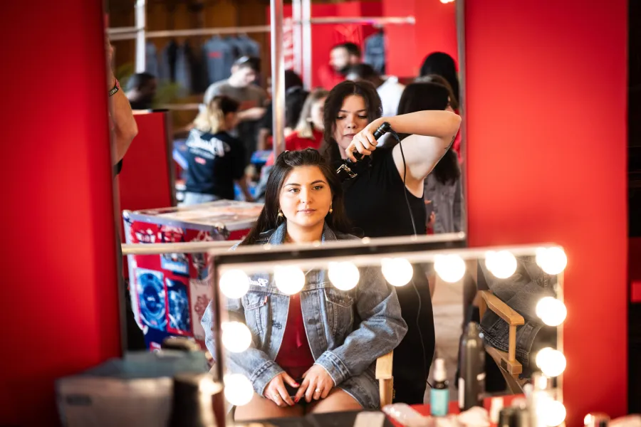 Guest at a lighted vanity while an artist styles her hair inside a red branded glam lounge