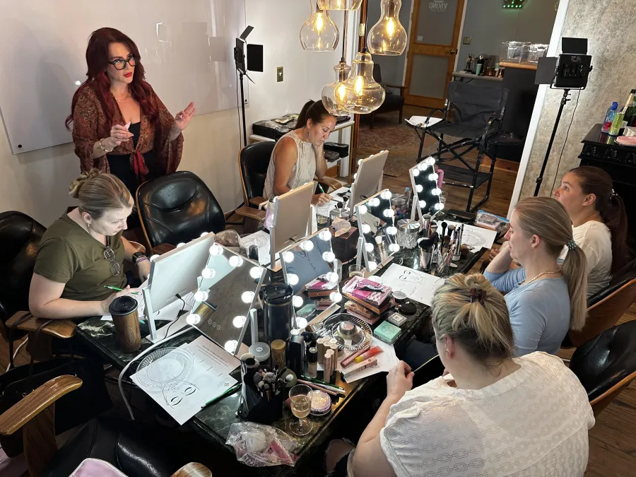 Group makeup lesson in progress: guests at lighted mirrors with Paula teaching
