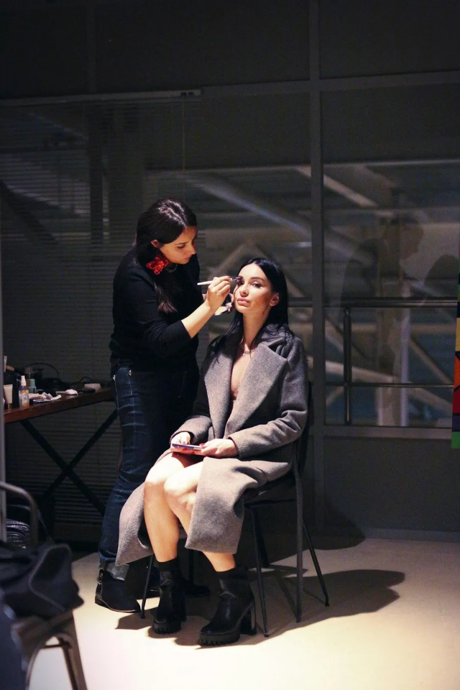 Makeup artist applying makeup to a seated model in a studio between setups