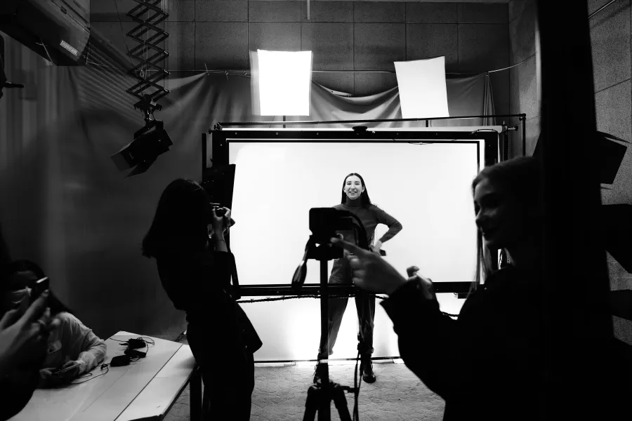 Black and white view of a studio set with lights, a white backdrop and a model mid-shoot