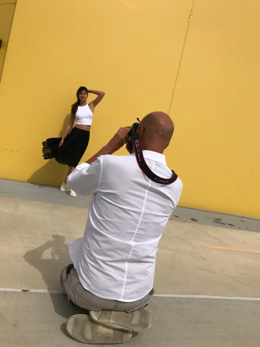 Photographer kneeling to shoot a model against a yellow wall on location
