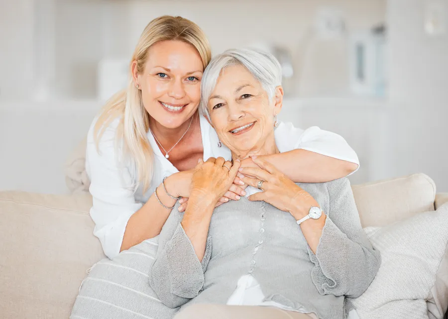 Adult daughter hugging her smiling mother on the sofa at home