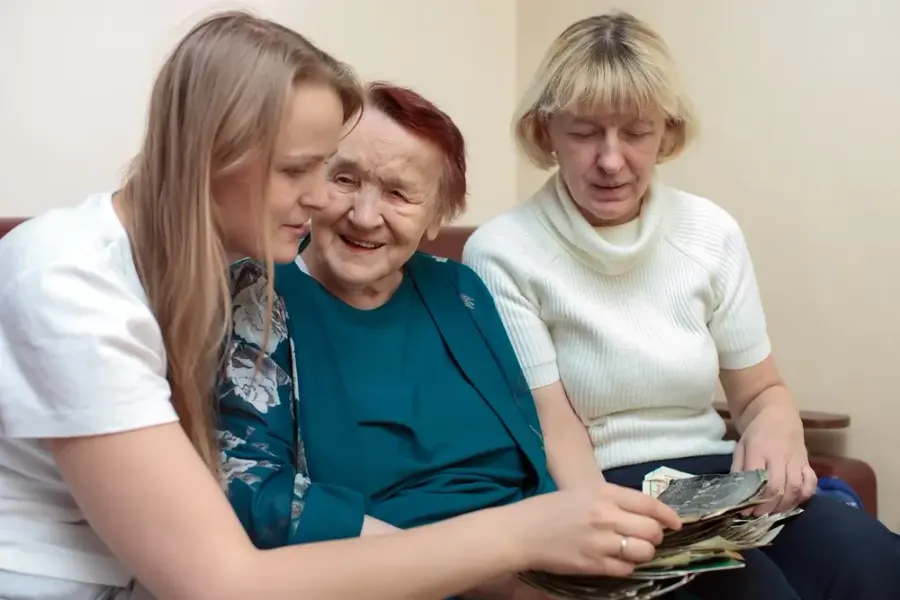 Two women looking through a photo album with a smiling senior woman