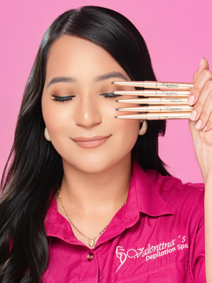 Especialista de Valentina's con camisa rosa sosteniendo lápices de cejas de la marca