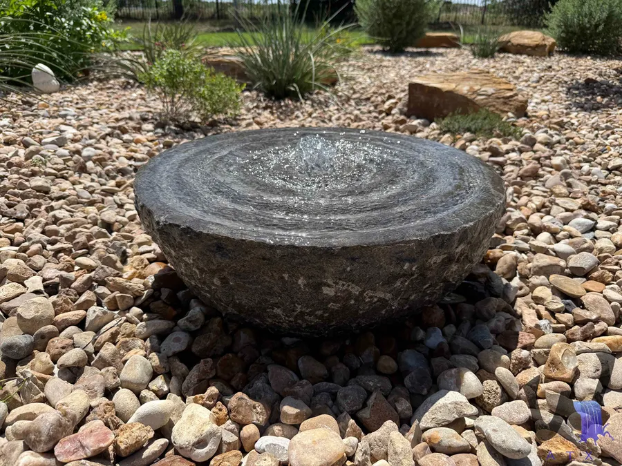 Stone fountain bowl installed in a gravel basin