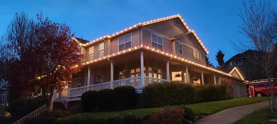 Two-story home with warm white roofline and porch lights at dusk