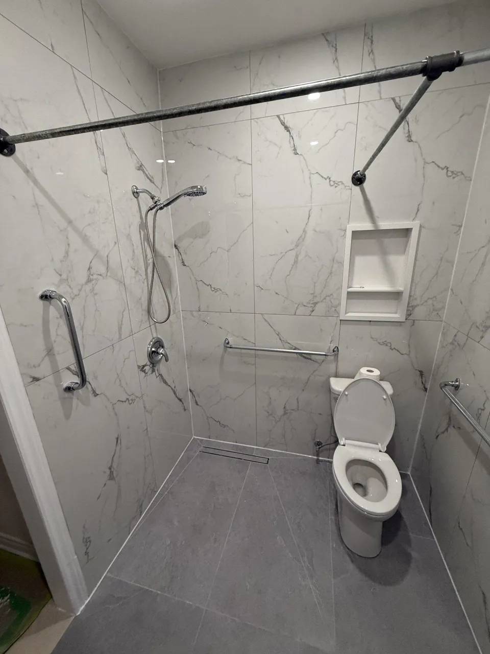 Walk-in shower with marble-look tile, grab bars and a built-in niche