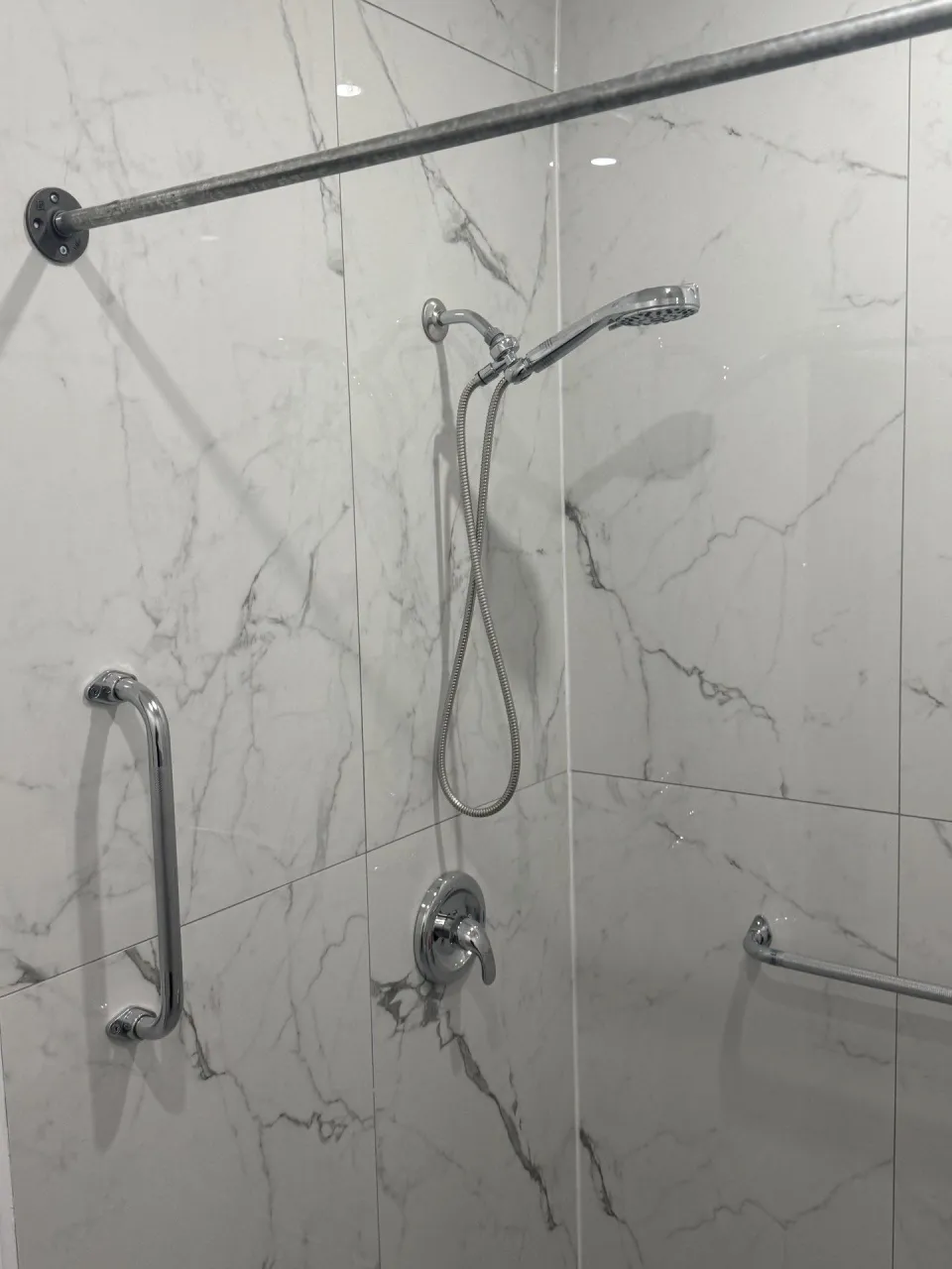Marble-look tiled shower with grab bars and handheld shower head