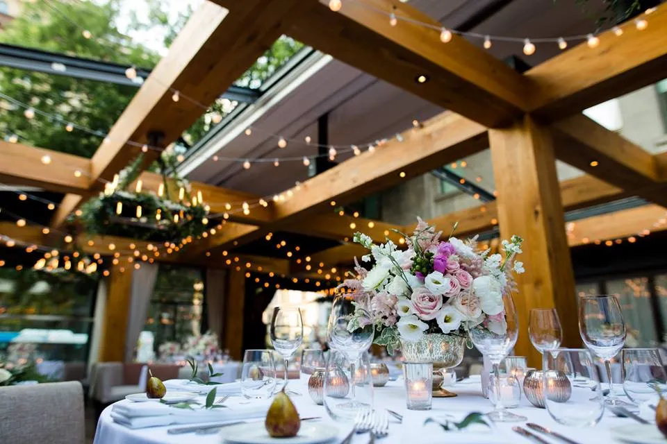 Réception de mariage extérieure sous une pergola avec centres de table lilas