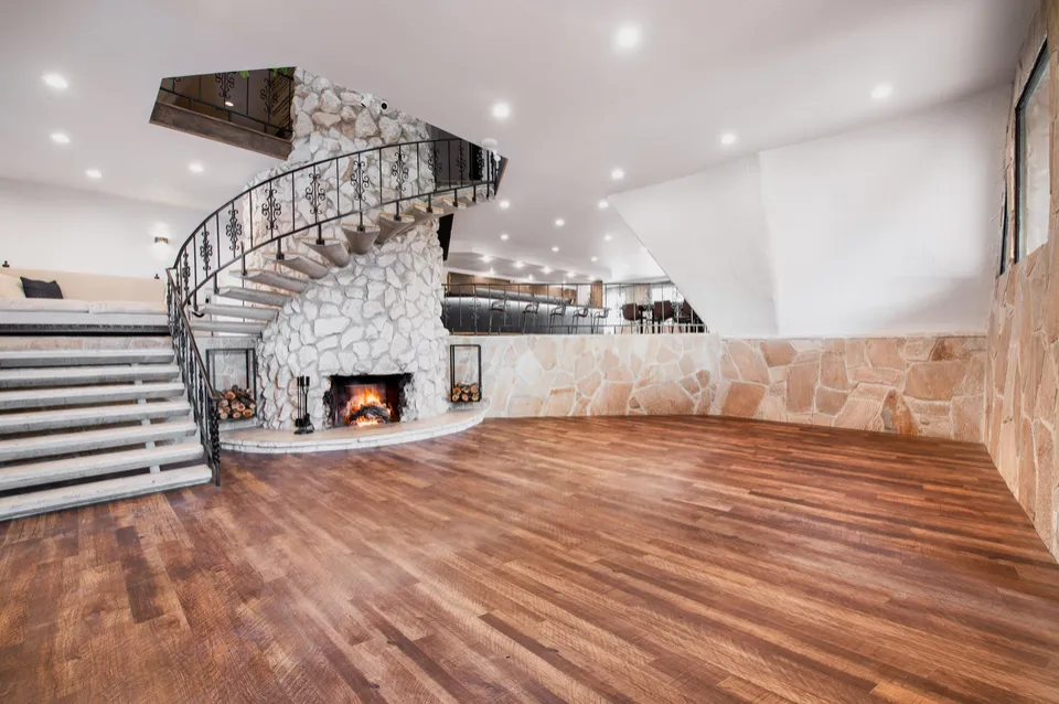 The Stone Crossing interior with its curved stone staircase, fireplace, wood floor, and bar above.