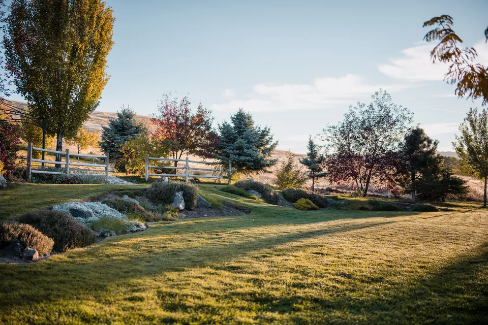 Landscaped gardens and lawn at Stone Crossing, framed by mature trees and a split-rail fence.