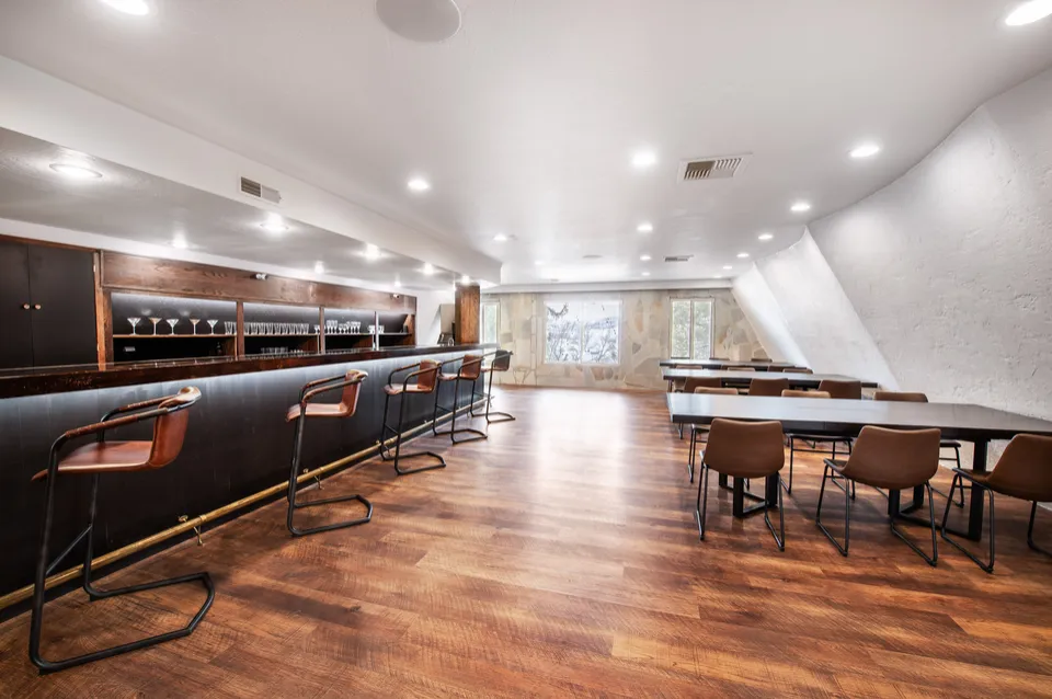 The estate bar with leather stools, wood finishes, and tables beside the windows.