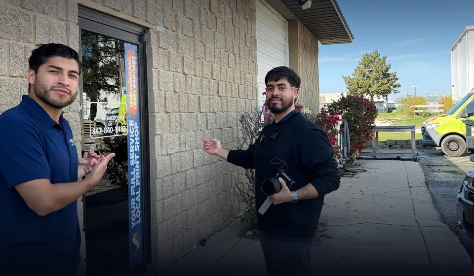 Angel and Cesar from VELPI outside a local business, one holding a camera